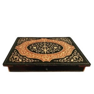 May include: A black wooden box with a decorative inlay of gold and brown floral patterns. The box has a hinged lid and a small keyhole.