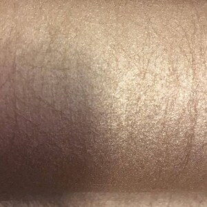 May include: Close-up of a shimmery, pearlescent, light brown eyeshadow with a smooth, slightly textured surface.