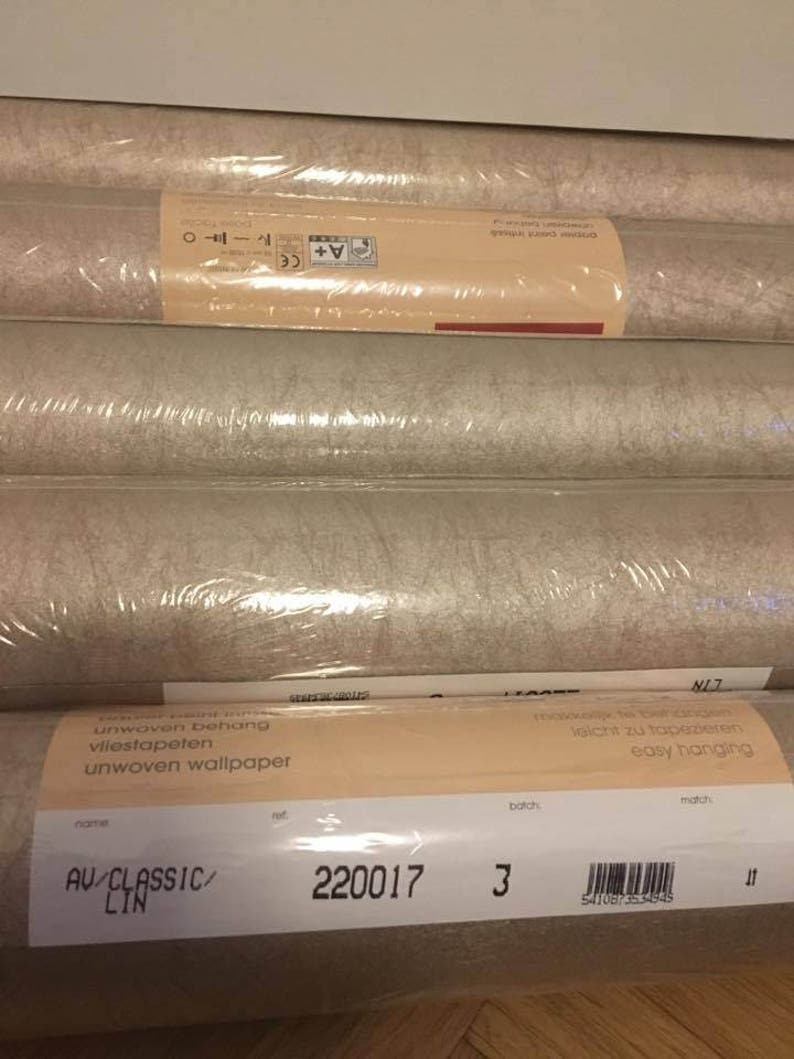 May include: A roll of beige wallpaper with the text "unwoven wallpaper" and "AV/CLASSIC/ LIN" on the label. The label also includes the batch number "3" and the product number "220017".