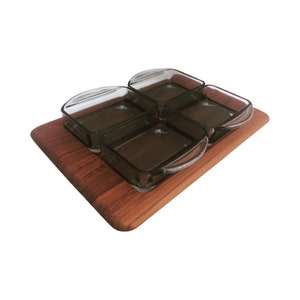 Puede incluir: Un juego de cuatro cuencos de vidrio transparente con asas, anidados en una bandeja de servir rectangular de madera. Los cuencos están dispuestos en un patrón cuadrado, con las asas hacia afuera.
