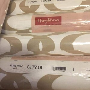 May include: A roll of white and beige wallpaper with a geometric pattern. The wallpaper is labeled "Heytens" and has the product number "617719".
