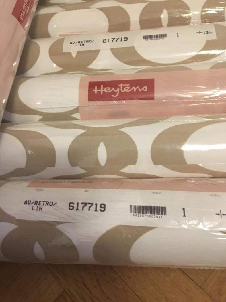 May include: A roll of white and beige wallpaper with a geometric pattern. The wallpaper is labeled "Heytens" and has the product number "617719".