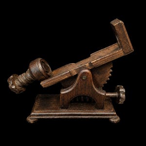 May include: A dark brown wooden book stand with an adjustable angled support, a central screw mechanism for height adjustment, a base with four small feet, and a side-mounted knob for controlling the tilt of the book rest platform.