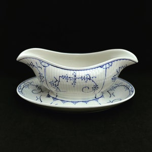 Può includere: Una salsiera in ceramica bianca con un motivo floreale blu e bianco. La salsiera è appoggiata su un sottopiatto abbinato.