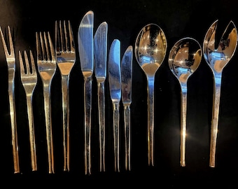 May include: A collection of polished silverware, including forks, knives, and spoons, arranged on a dark surface. The set includes various fork styles, multiple knives, and spoons, with a salad fork and spoon. The silverware has a reflective, metallic finish.
