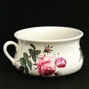 Op de afbeelding: Witte keramische kom met een handvat, met een bloemenontwerp van roze rozen en groene bladeren.