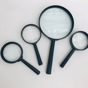 K&ouml;nnte beinhalten: Vier Lupen in verschiedenen Gr&ouml;&szlig;en, alle schwarz mit klaren Glaslinsen. Die gr&ouml;&szlig;te Lupe befindet sich in der Mitte des Bildes, die anderen drei sind um sie herum angeordnet.