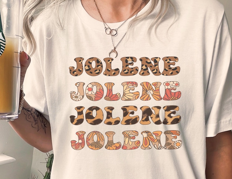 May include: A white short-sleeved t-shirt featuring the name JOLENE printed four times in a stacked design. The first and third lines have a brown and black leopard print pattern, while the second and fourth lines feature a floral pattern.