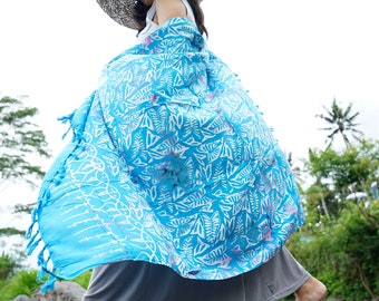 May include: A woman wearing a straw hat and a blue and white patterned sarong walks across rocks in a stream.