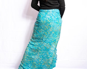 May include: A long, flowing turquoise skirt with a gold, swirling pattern. The skirt is paired with a black long-sleeve top. The fabric appears soft and drapes elegantly. The skirt's design suggests a bohemian or resort style.