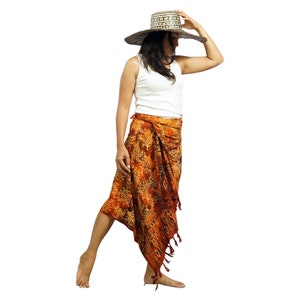 May include: A woman wearing a white tank top and a brown and white patterned sarong skirt. She is wearing a wide-brimmed straw hat and is looking down.