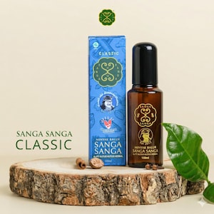 May include: A brown glass bottle and a blue box of Sanga Sanga Classic herbal oil. The bottle has a black cap and a gold label. The box features a logo and text in Indonesian. The products are displayed on a wooden slice.