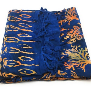 May include: A blue and orange batik sarong with fringe. The sarong has a floral pattern and is made of a soft, lightweight fabric.