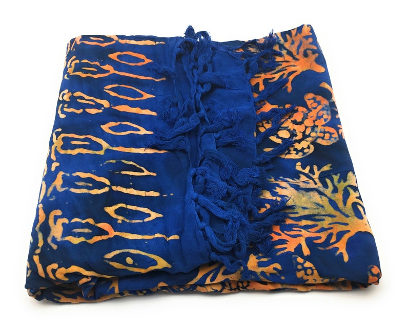 May include: A blue and orange batik sarong with fringe. The sarong has a floral pattern and is made of a soft, lightweight fabric.