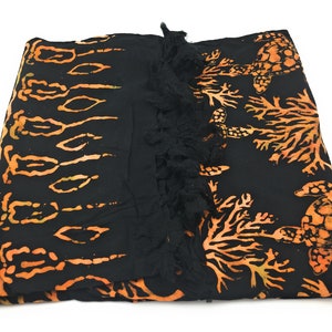 May include: Black sarong with orange and yellow batik print of sea turtles and coral. The sarong has a black fringe trim.