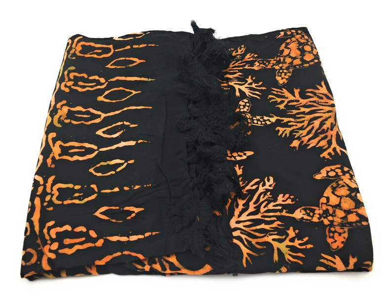 May include: Black sarong with orange and yellow batik print of sea turtles and coral. The sarong has a black fringe trim.