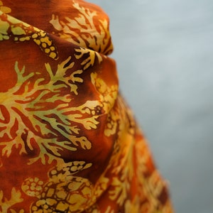 May include: A close-up of a rust-colored scarf with a yellow and brown floral pattern. The pattern features sea turtles and coral.