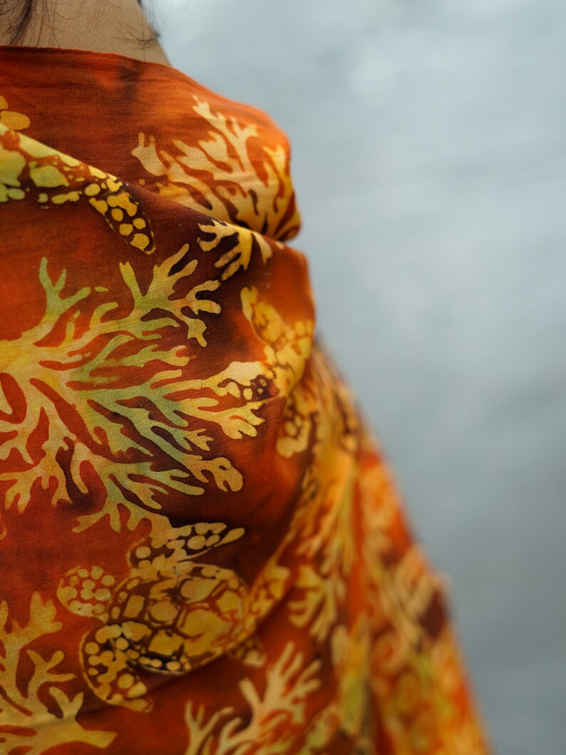 May include: A close-up of a rust-colored scarf with a yellow and brown floral pattern. The pattern features sea turtles and coral.