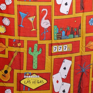 May include: A red and yellow fabric with a repeating pattern of Las Vegas themed images. The images include a flamingo, a cactus, a guitar, dice, playing cards, a martini glass, and a sign that says "Welcome to Fabulous Las Vegas".