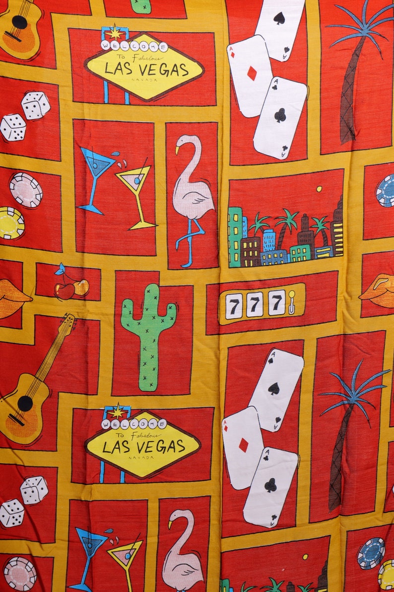 May include: A red and yellow fabric with a repeating pattern of Las Vegas themed images. The images include a flamingo, a cactus, a guitar, dice, playing cards, a martini glass, and a sign that says "Welcome to Fabulous Las Vegas".