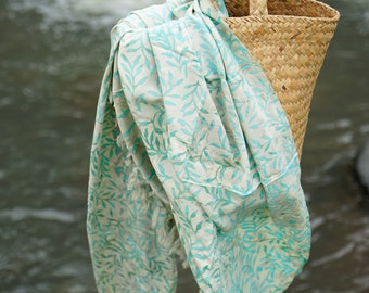 May include: A white and turquoise patterned sarong draped over a woven wicker basket with a handle.