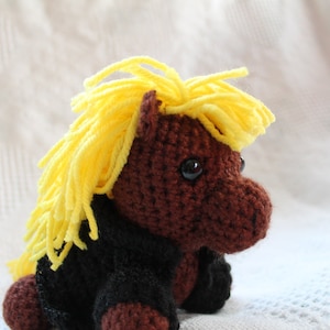 May include: A brown crocheted pony with yellow yarn hair wearing a black crocheted jacket.