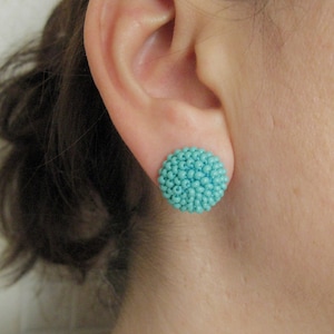 May include: A pair of turquoise blue beaded earrings. The earrings are round and have a textured surface.