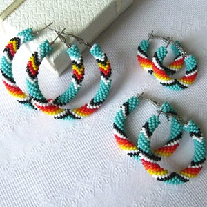 Könnte beinhalten: Drei Paar türkisfarbene, weiße, schwarze, rote und gelbe Perlen-Creolen. Die Ohrringe sind in verschiedenen Größen.