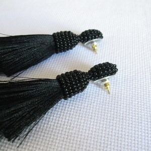 May include: A pair of black tassel earrings with black bead detailing. The earrings have a post back closure.