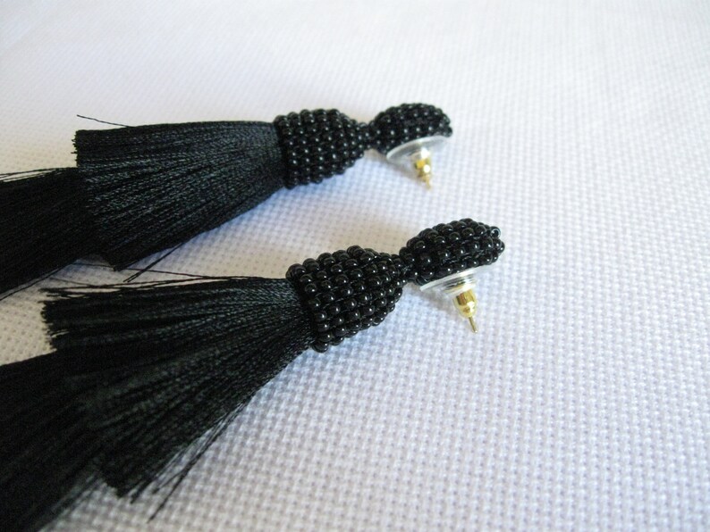 May include: A pair of black tassel earrings with black bead detailing. The earrings have a post back closure.