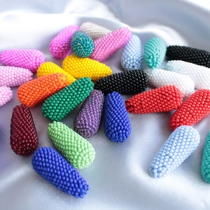 Könnte beinhalten: Eine Sammlung von bunten, tropfenförmigen Perlenornamenten. Die Ornamente bestehen aus kleinen Perlen in verschiedenen Farben, darunter Rosa, Lila, Blau, Grün, Rot, Orange, Gelb und Weiß.