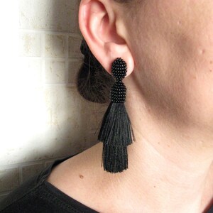 May include: Black tassel earrings with a beaded top. The earrings are long and dangle from the earlobe.