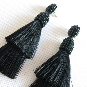 May include: A pair of black tassel earrings with black bead accents. The earrings are made of silk and have a layered tassel design.