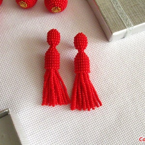 May include: A pair of red beaded tassel earrings. The earrings are about 2 inches long and have a small red bead at the top.