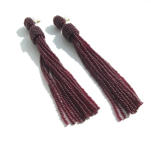 May include: A pair of long, burgundy tassel earrings. The tassels are made of small beads and are attached to a gold-toned post.