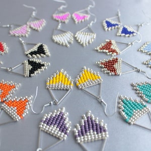 May include: A collection of 10 pairs of triangle-shaped earrings made with silver-toned metal and colorful beads. The earrings are arranged in a circle on a silver surface.