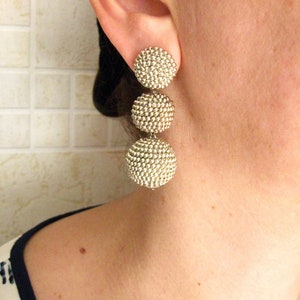 May include: Silver tone dangle earrings with three round beads. The beads are made of small, closely packed silver balls. The earrings are labeled "Medium Color #3".