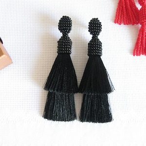 May include: A pair of black tassel earrings with a beaded top. The tassels are layered and have a fringe-like appearance.