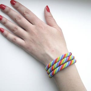 Op de afbeelding: Drie regenboogkleurige kralenarmbanden gestapeld op iemands pols.