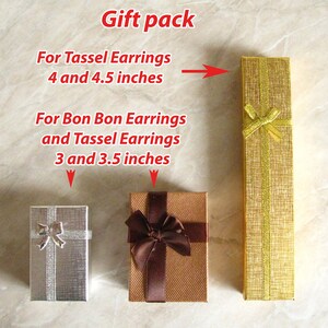 May include: Three gift boxes for earrings. The boxes are made of brown and silver cardboard with a gold ribbon. The boxes are labeled with the text "For Tassel Earrings 4 and 4.5 inches" and "For Bon Bon Earrings and Tassel Earrings 3 and 3.5 inches".