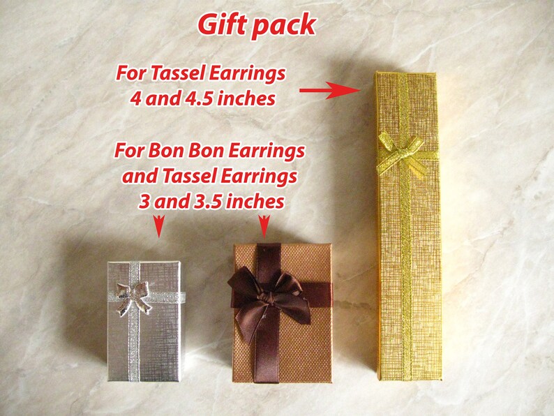 May include: Three gift boxes for earrings. The boxes are made of brown and silver cardboard with a gold ribbon. The boxes are labeled with the text "For Tassel Earrings 4 and 4.5 inches" and "For Bon Bon Earrings and Tassel Earrings 3 and 3.5 inches".