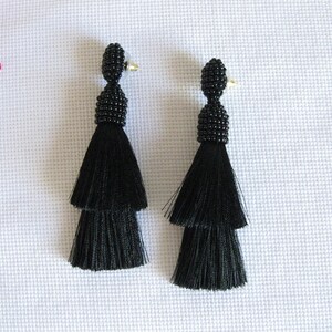 May include: A pair of black tassel earrings with a beaded top. The tassels are two-tiered and the beads are small and black.