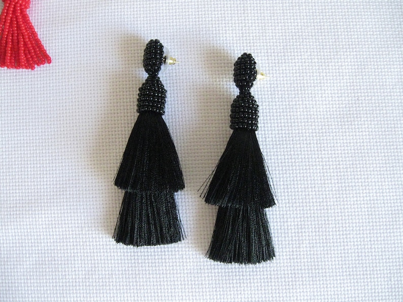 May include: A pair of black tassel earrings with a beaded top. The tassels are two-tiered and the beads are small and black.