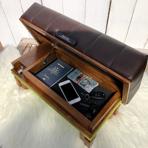 May include: A wooden storage bench with a brown leather top. The top lifts to reveal a storage compartment with a passport, cash, a phone, and keys inside. The bench has a green accent around the edge.