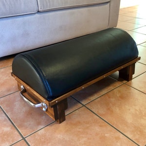 May include: A black leather footstool with a wooden frame and a silver handle. The footstool has a rounded top and is supported by four legs.