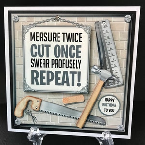 Op de afbeelding: Een vierkante wenskaart met een bakstenen achtergrond en een centraal bord met de tekst MEASURE TWICE CUT ONCE SWEAR PROFUSELY REPEAT! Illustraties bevatten een metalen liniaal, een hamer, een handzaag, een pleister en een cirkel met HAPPY BIRTHDAY TO YOU.