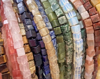 May include: A collection of colorful gemstone beads, each strand featuring square-shaped beads in various colors, including pink, green, blue, brown, and white.