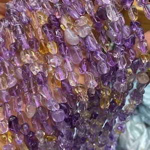 May include: Strands of polished gemstone beads in shades of purple and yellow. The beads are irregular in shape and appear to be amethyst and citrine. The gemstones are strung together, ready for jewelry making or crafting.