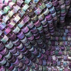 Könnte beinhalten: Eine Strähne runder, facettierter Edelsteinperlen in Violett-, Grün- und Blautönen. Die Perlen sind in einem sich wiederholenden Muster angeordnet, wodurch eine optisch ansprechende Textur entsteht.