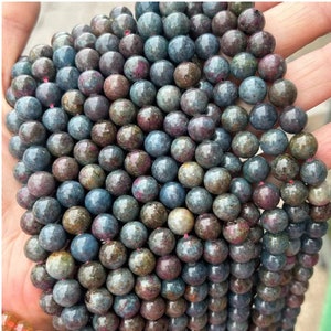 May include: A strand of round, multi-colored gemstone beads. The beads are a mix of blue, green, and pink hues. The beads are strung on a thin, red thread.